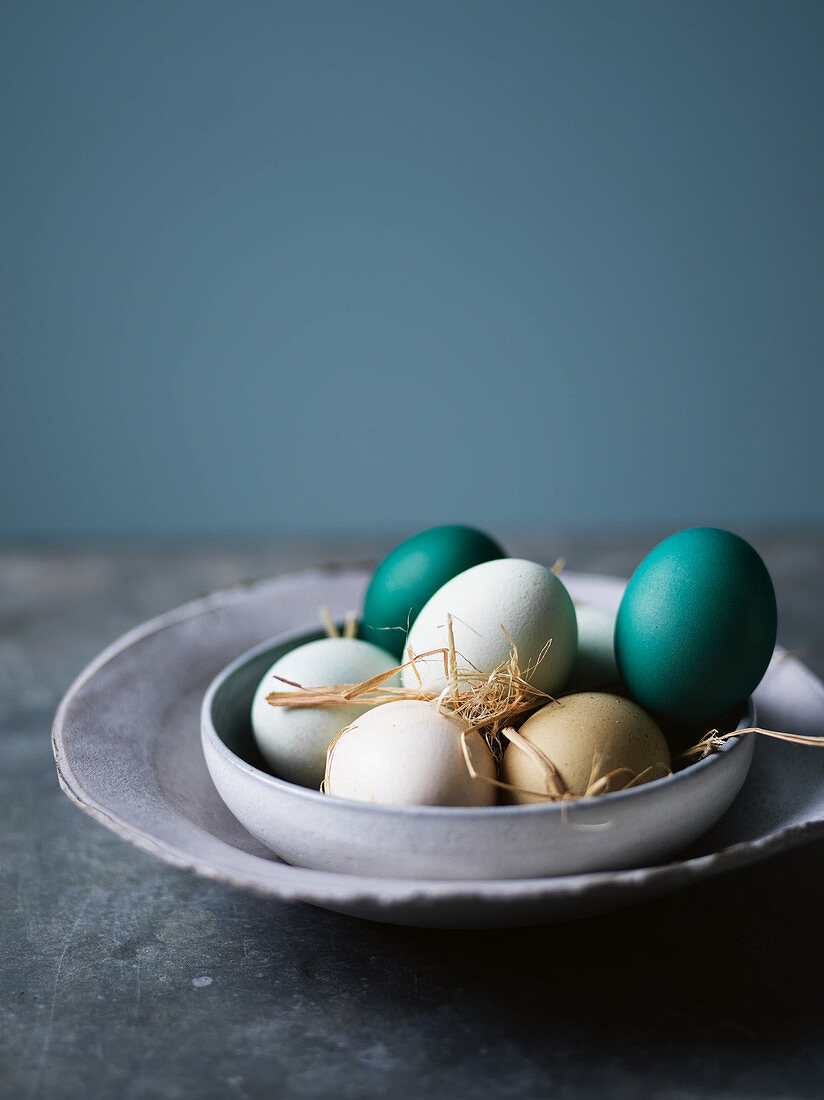 Various coloured eggs with straw in a ceramic bowl
