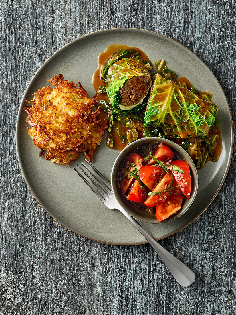Savoy cabbage and game roulade with potato fritters and tomato salad