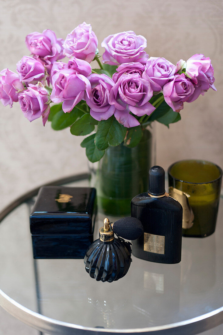 Vase of purple roses, perfume and jewellery box on side table