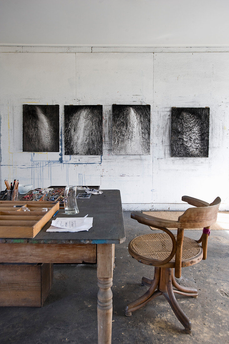 Wooden table and chair in front of modern artworks on wall of study