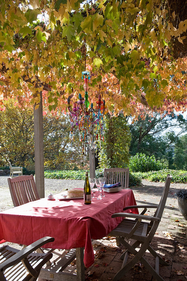 Table with red tablecloth and wooden chairs below chair with autumn foliage