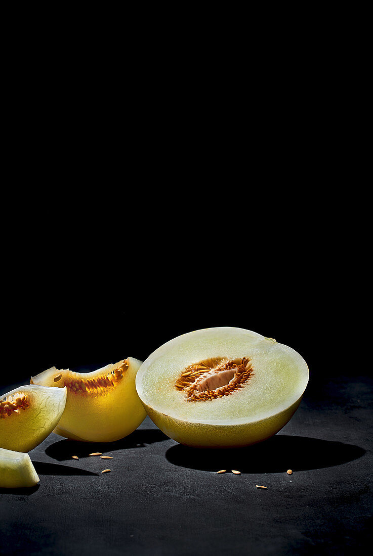 Bisected ripe fresh melon with seeds and tasty pieces under light in dark room