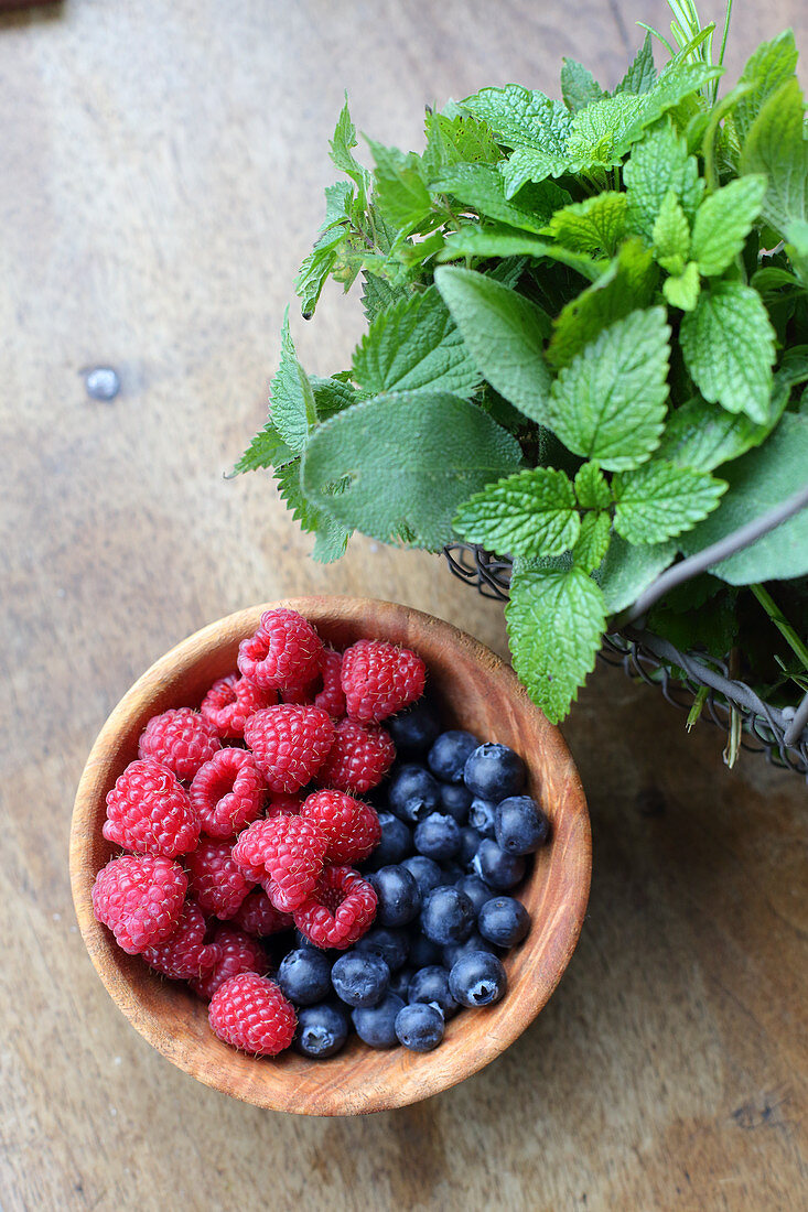 Berries in a wooden bowl next to a wire basket of herbs