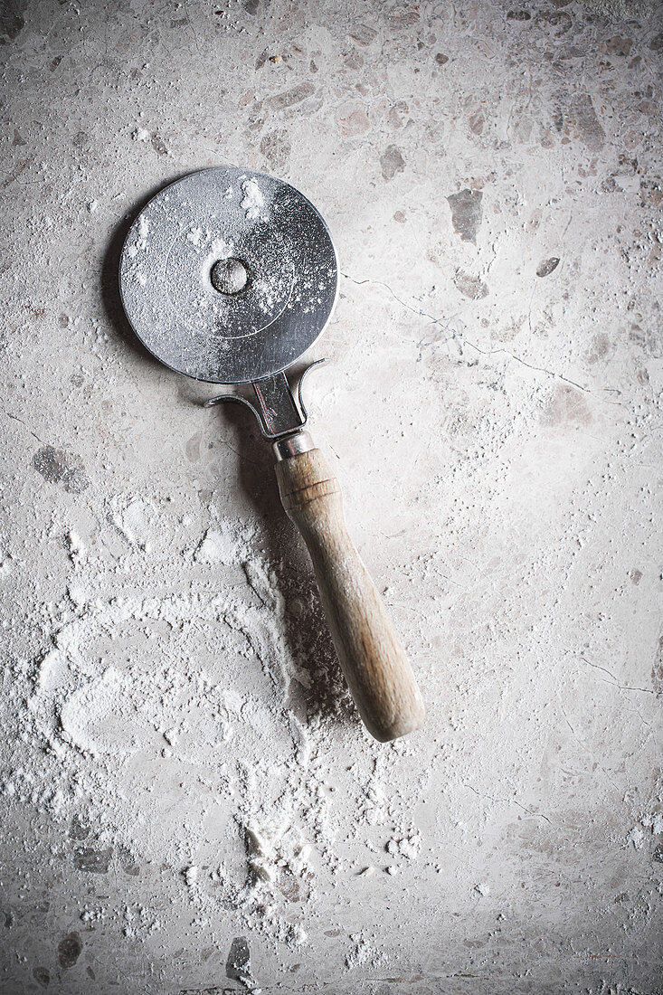 A pizza cutter and flour on a stone surface