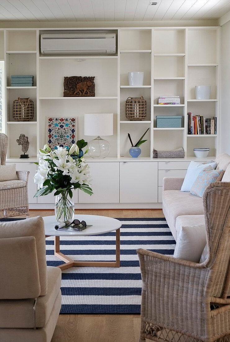 White fitted shelving in seating area with pale rattan and upholstered furniture