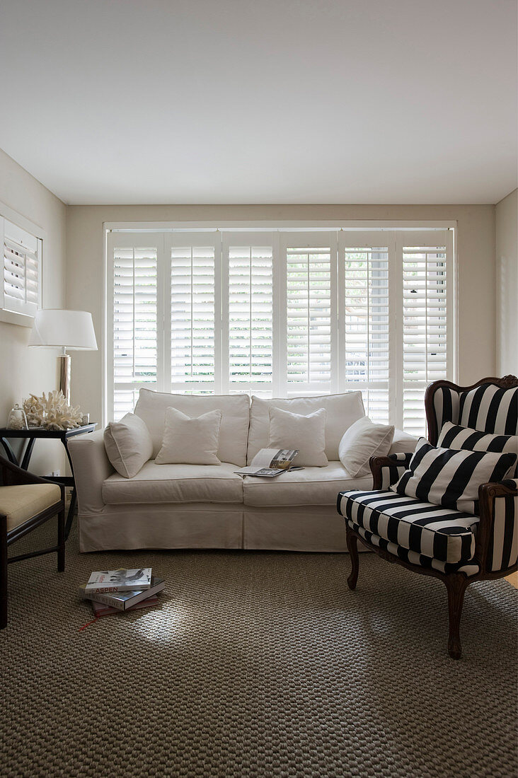 Armchairs and two-seater sofa in front of glass wall with louvre blinds