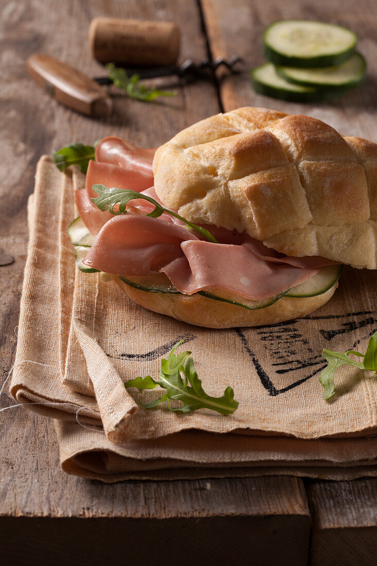 A bread roll with mortadella, cucumber and rocket