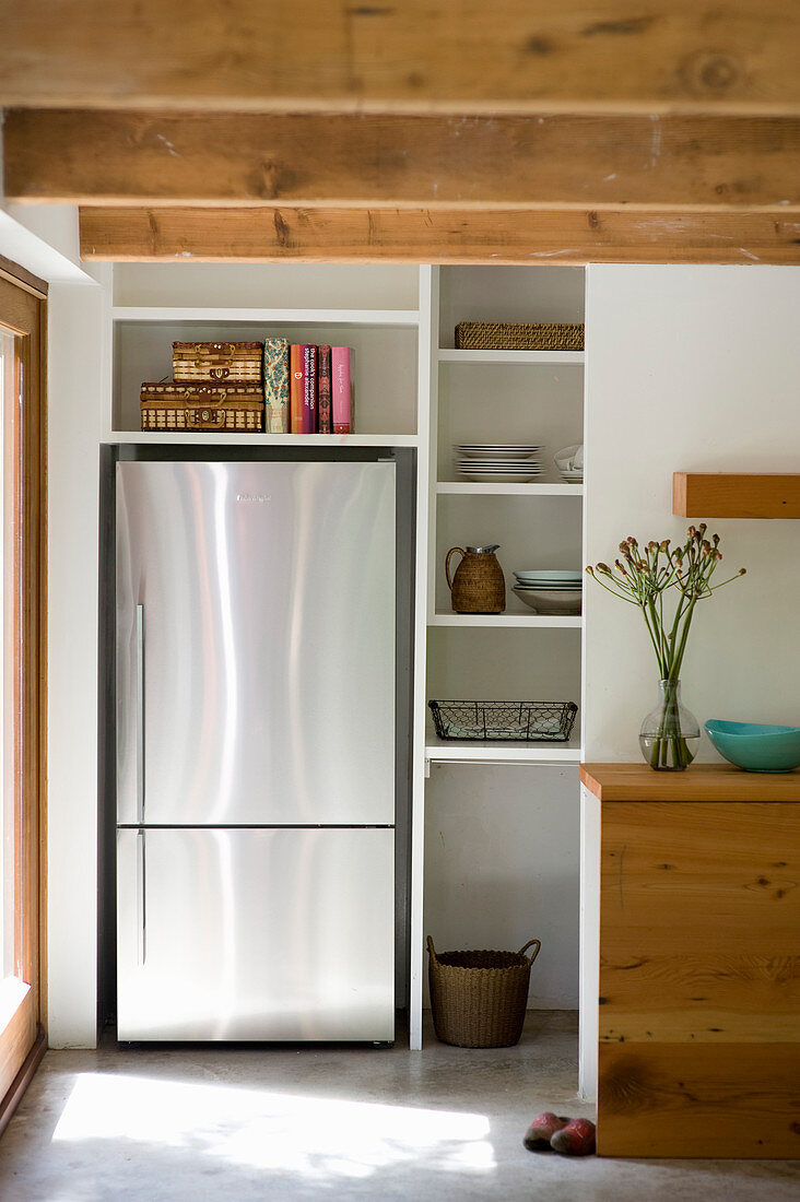 Modern stainless steel fridge in niche next to kitchen shelves