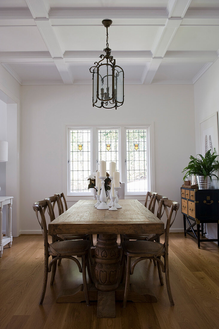 Solid wooden dining table in elegant, white interior with coffered ceiling