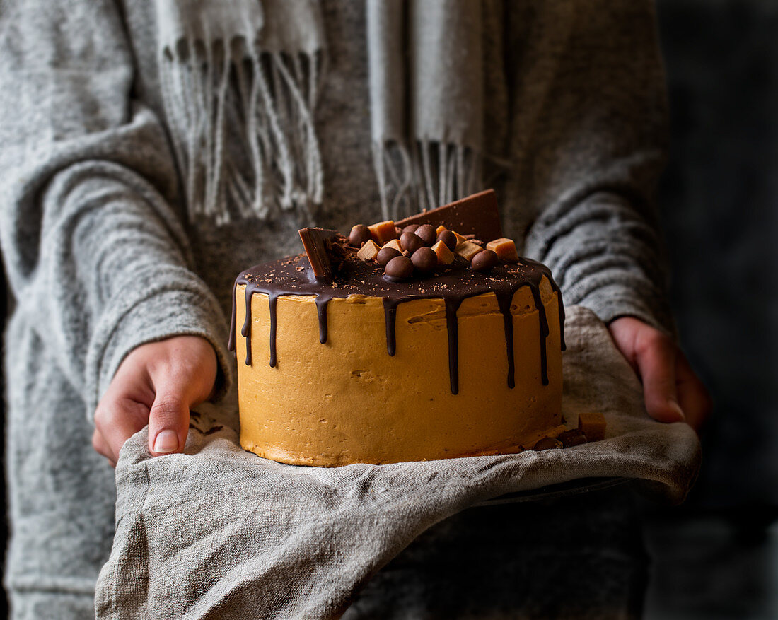 Chocolate and salted caramel cake with hands holding it
