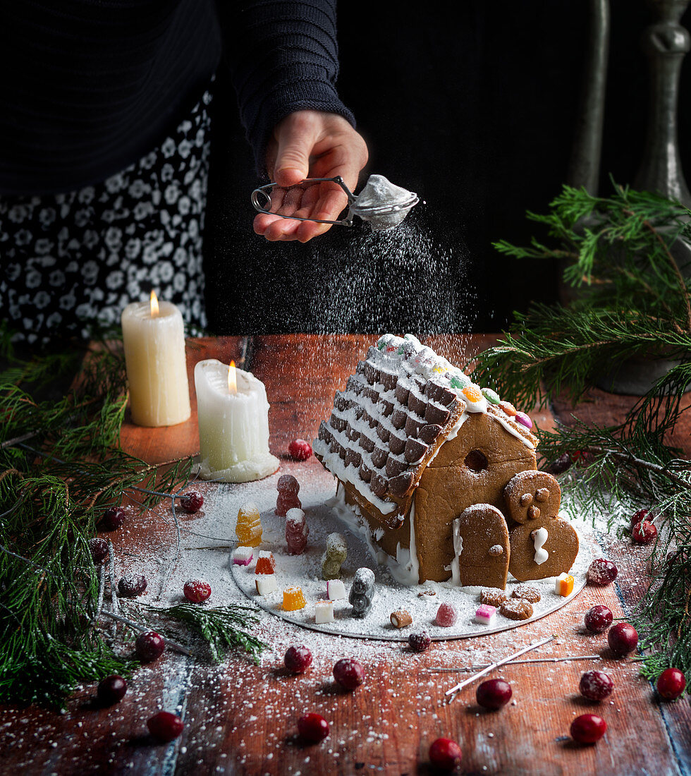 Lebkuchenhaus mit Puderzucker bestreuen