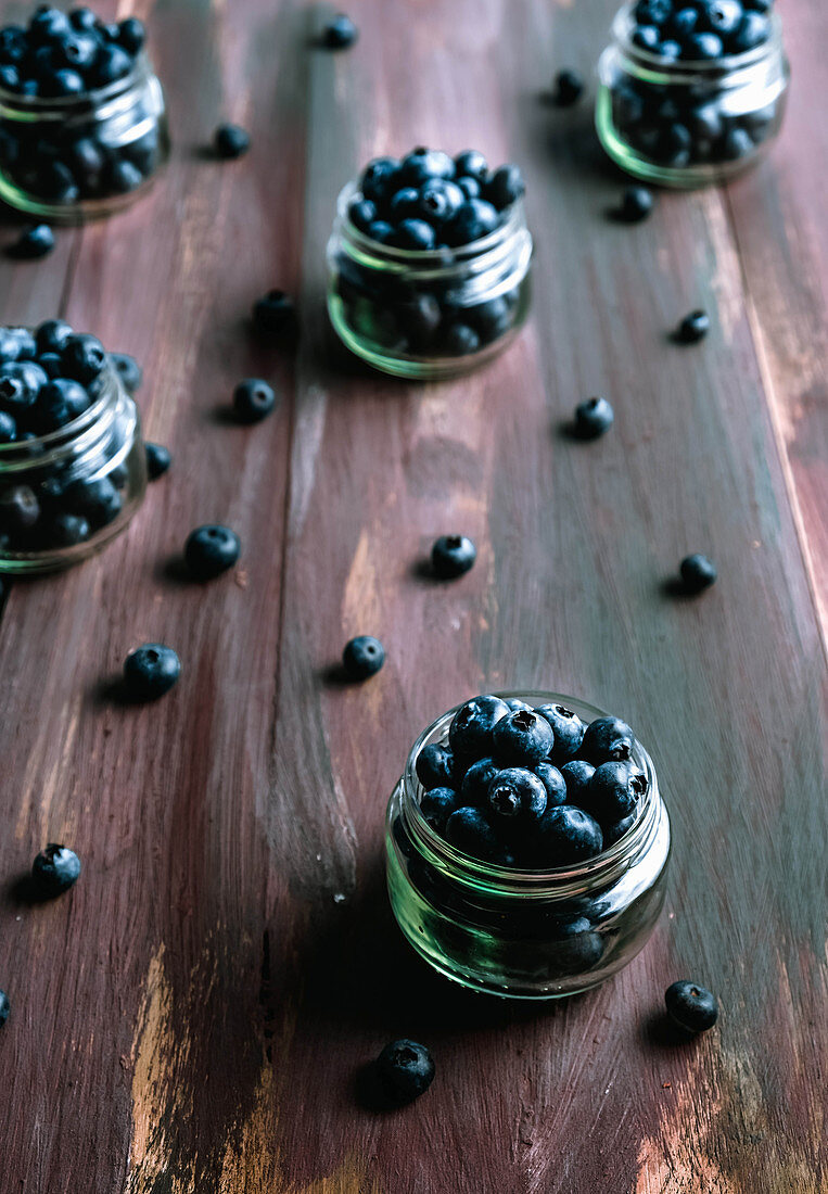 Frische Blaubeeren in Schraubgläschen und auf Holzuntergrund