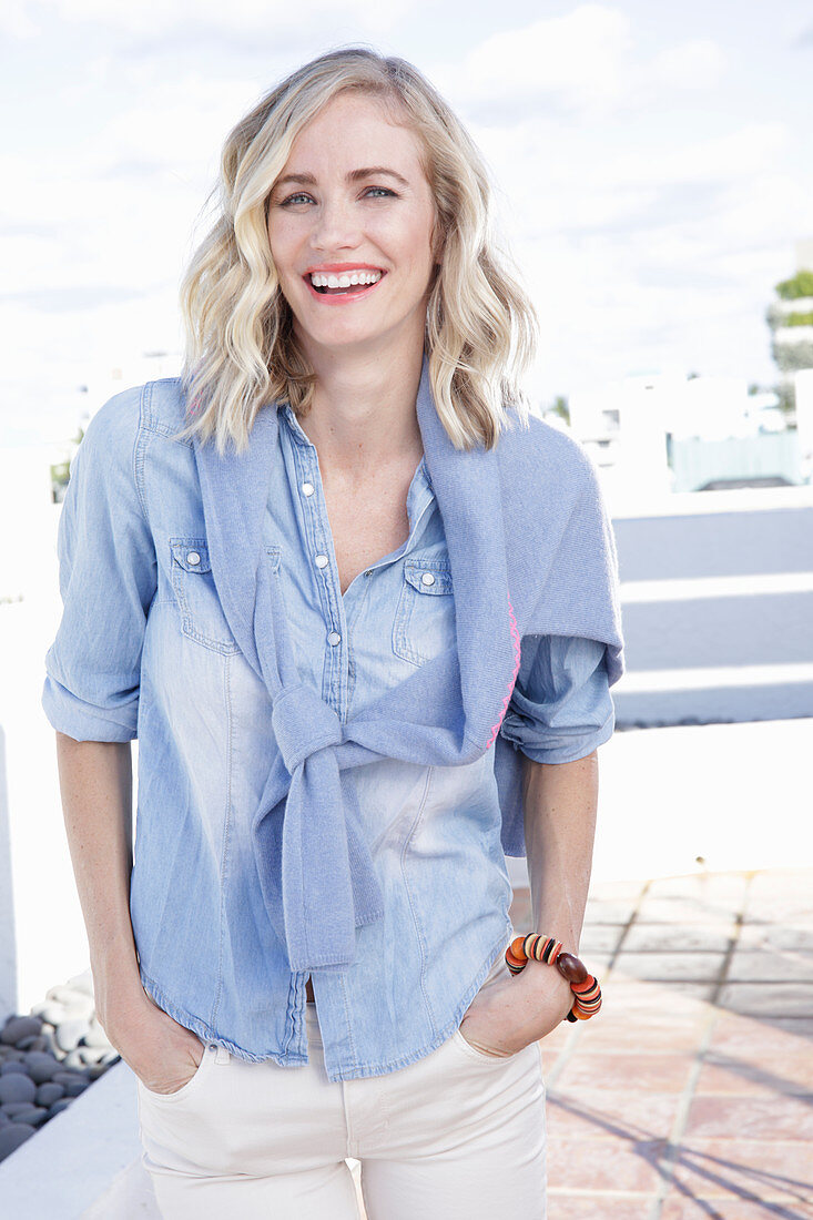 A blonde woman wearing a denim shirt with a jumper over her shoulders