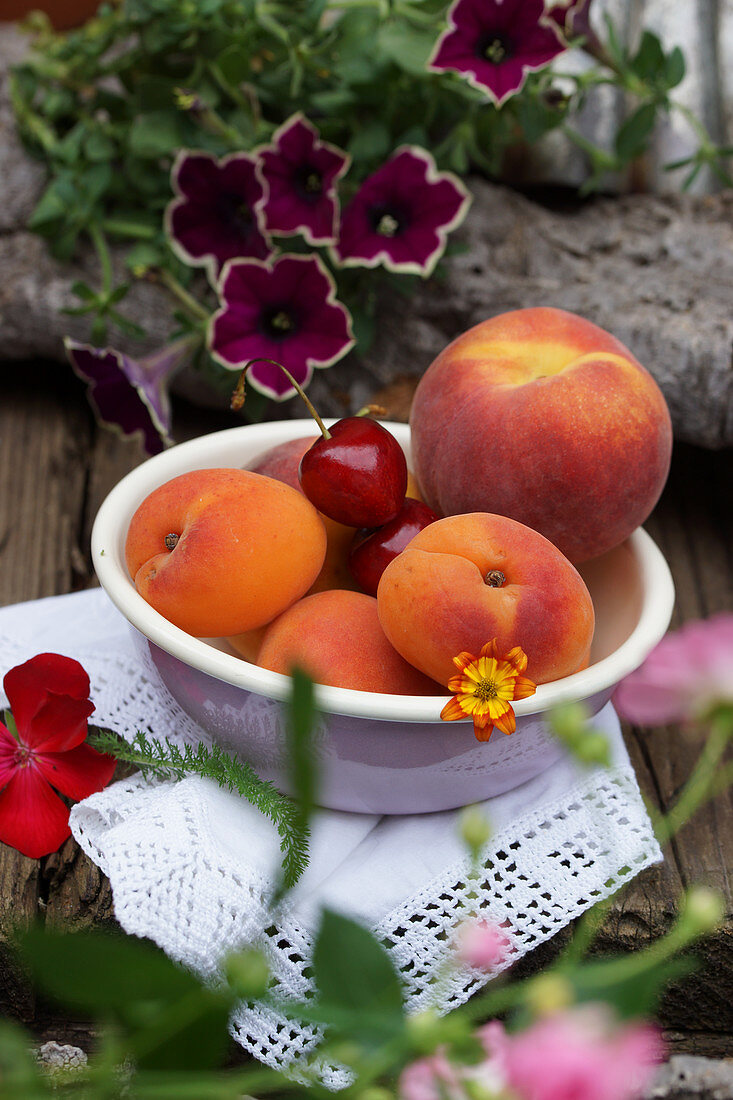 A fruit bowl with apricots, peach and sweet cherries