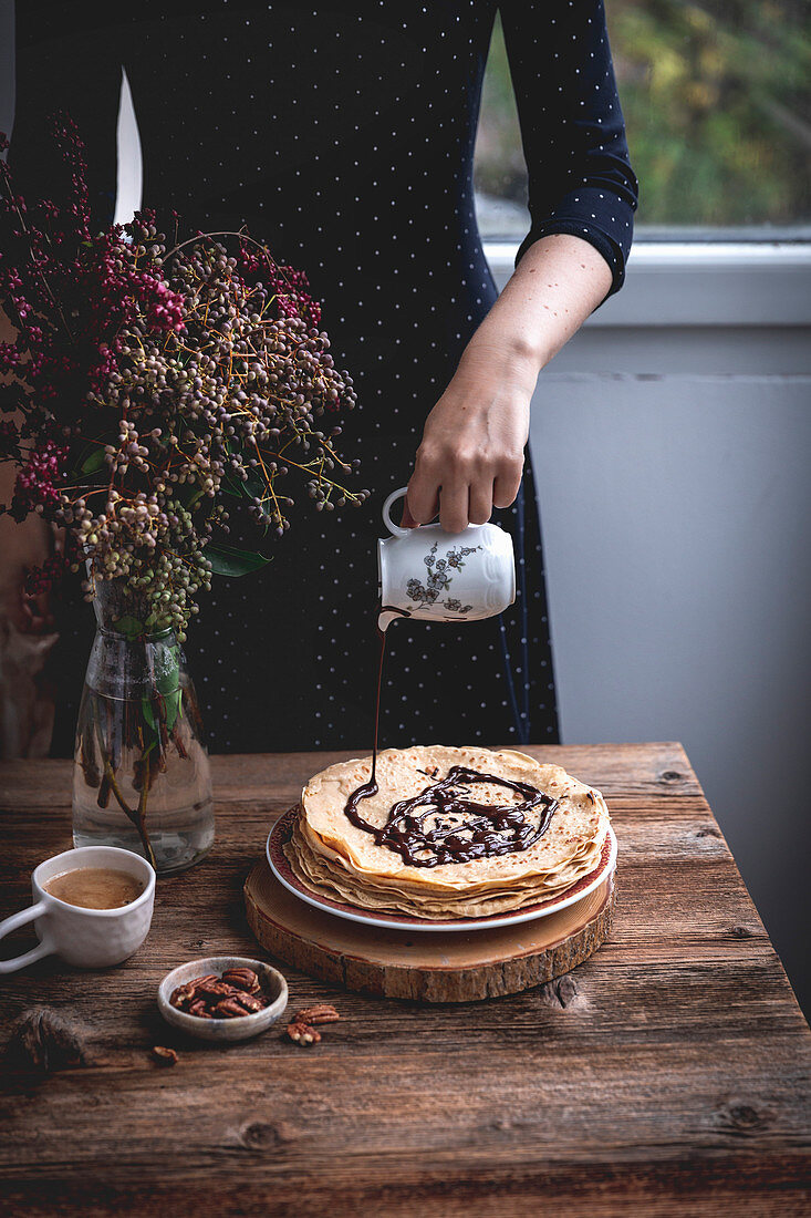 Woman pouring melted dark chocolate on a stack of crepes