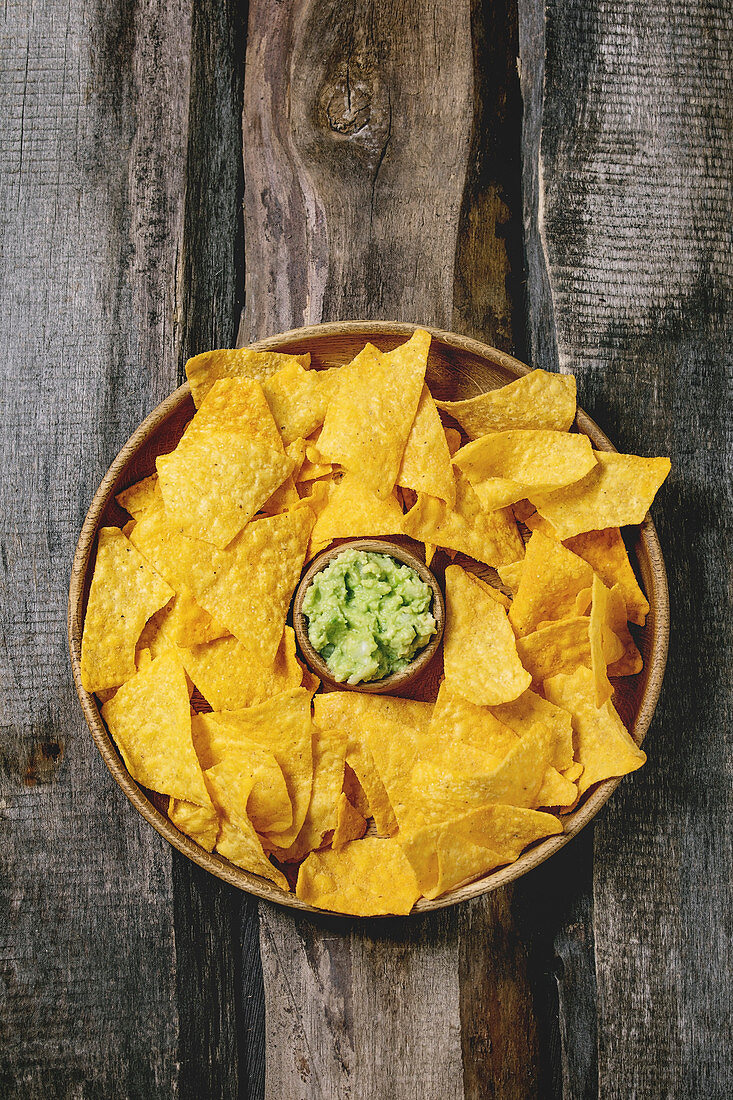 Tortilla nachos corn chips with avocado guacamole sauce served in wood plate