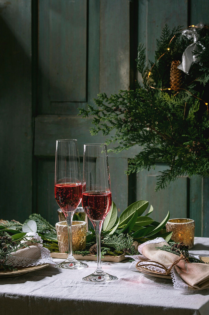 Christmas or New year table setting with empty ceramic plates, wine glasses, napkins, Christmas thuja wreath, luminous garland and burning candles