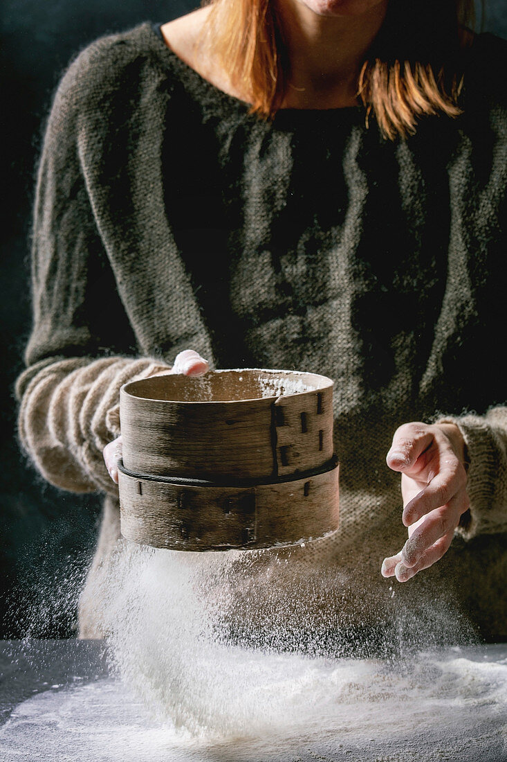 Process of making homemade bread dough: Woman hands sifts flour from vintage sieve