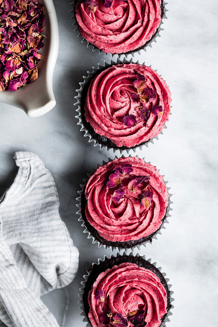 Schokoladen-Cupcakes mit rosa Frosting und getrockneten Rosenblättern