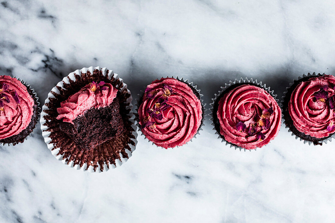 Schokoladen-Cupcakes mit rosa Frosting, einer angebissen