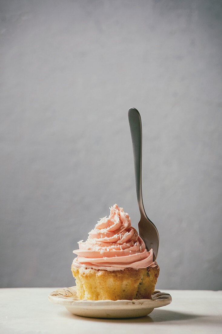 Ein Cupcake mit rosa Buttercreme-Frosting vor grauem Hintergrund