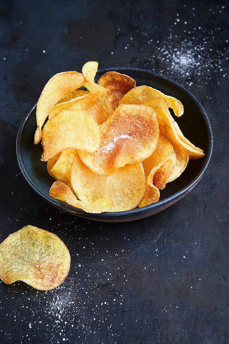 Homemade Potato Chips on Paper; Bowl of Salt