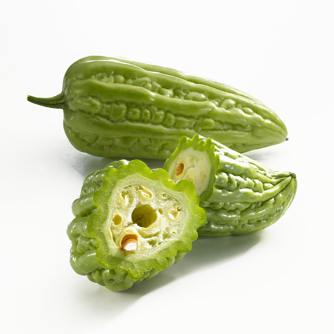 A whole and a halved bitter cucumber on a white background