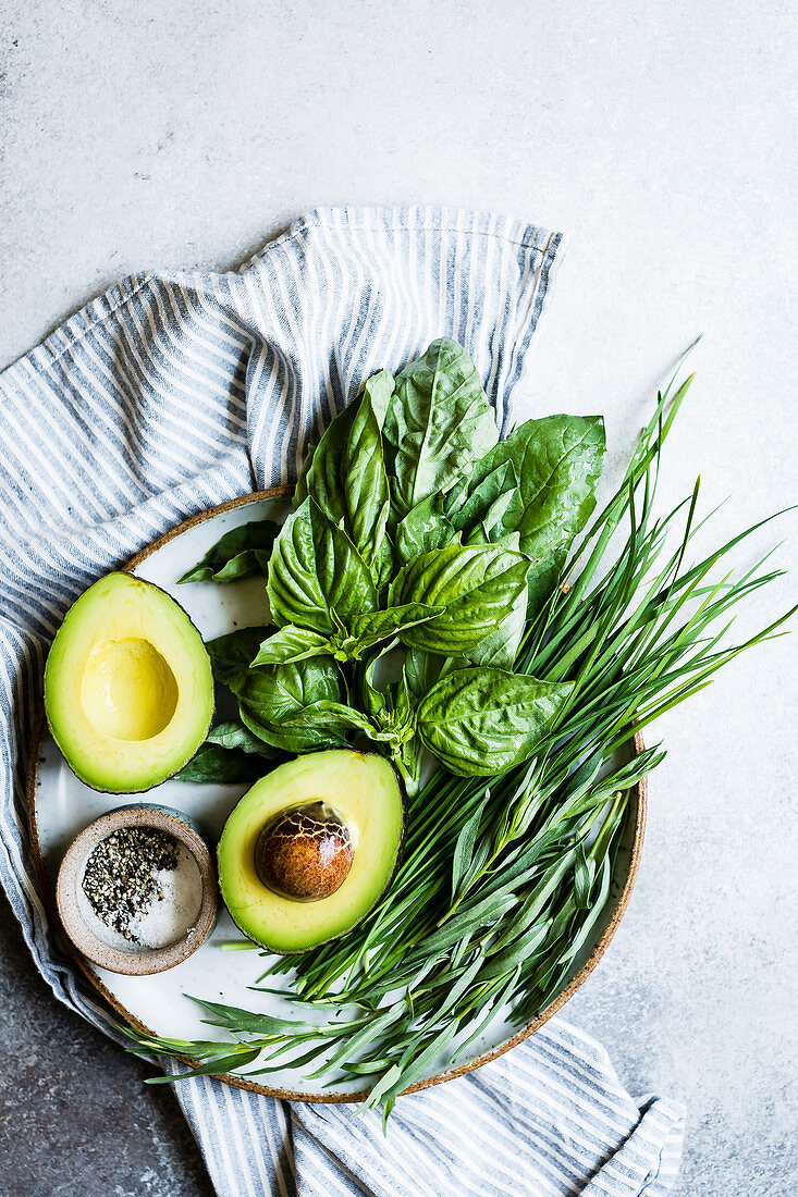 Halbierte Avocado, Salz, Pfeffer und frische Käuter auf Teller