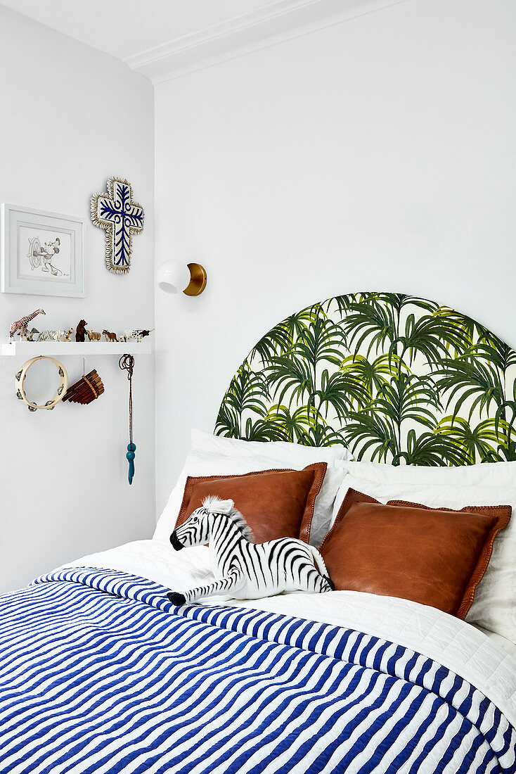 Bed with blue-and-white striped bed linen and exotic leaf pattern on headboard