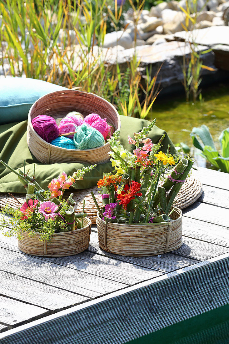 Gestecke mit Knöterich, Zinnien und Löwenmäulchen in Körben auf einem Steg