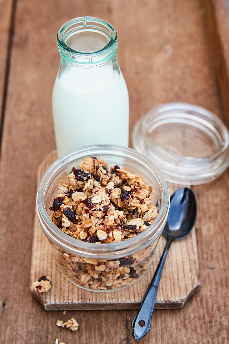 Granola with dried cranberries in a glass jar in front of a milk bottle
