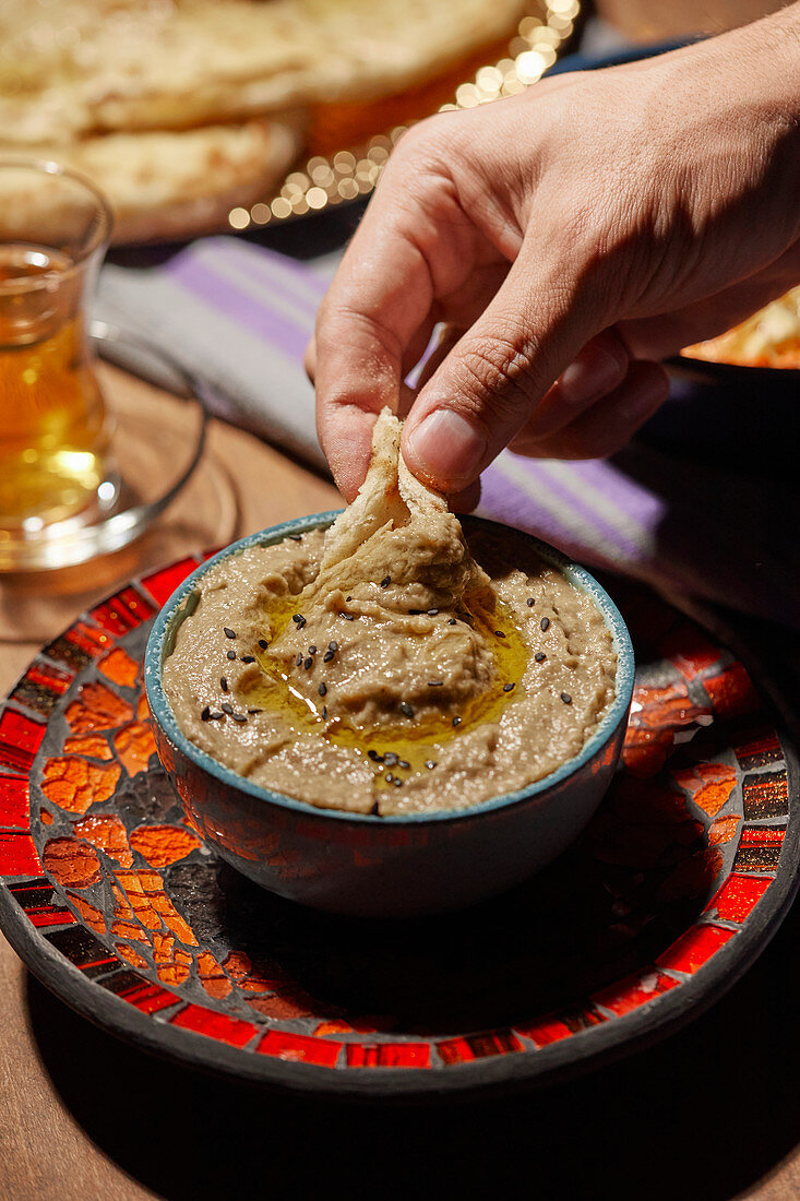 Ein Stück Brot in Baba-Ghanoush-Dip eintauchen