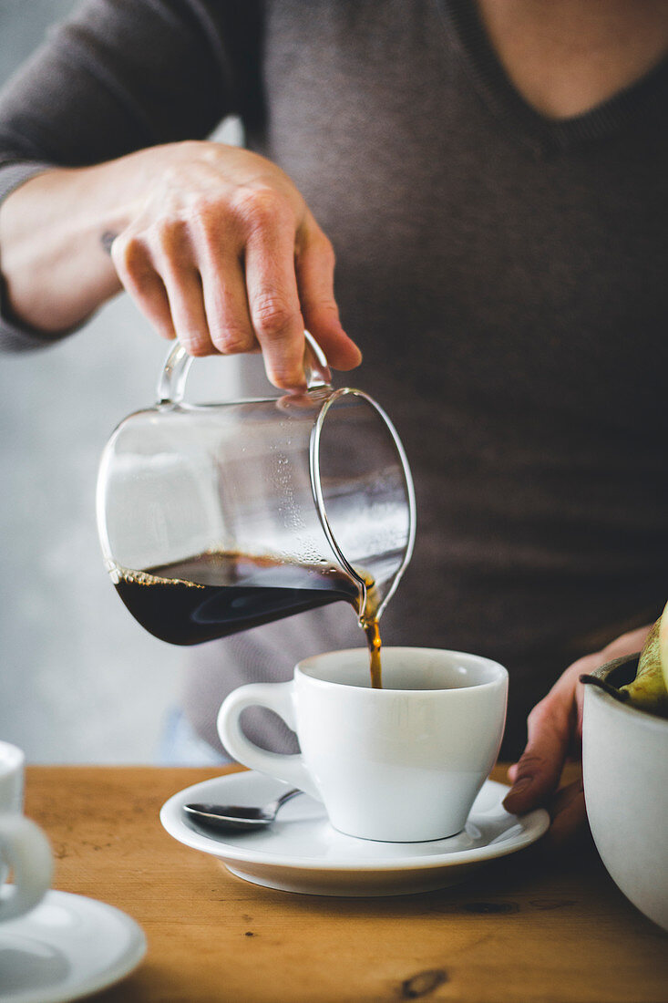 Frauenhand giesst Kaffee in Kaffeetasse
