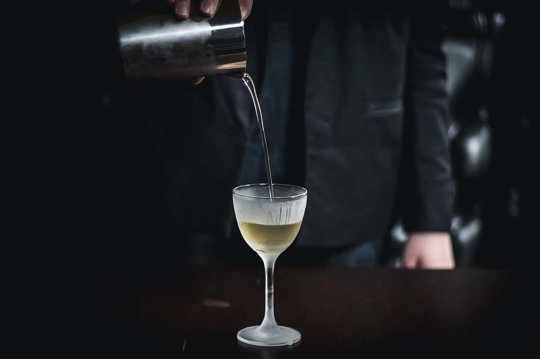 Pouring a clear coffee cocktail from a shaker into a glass