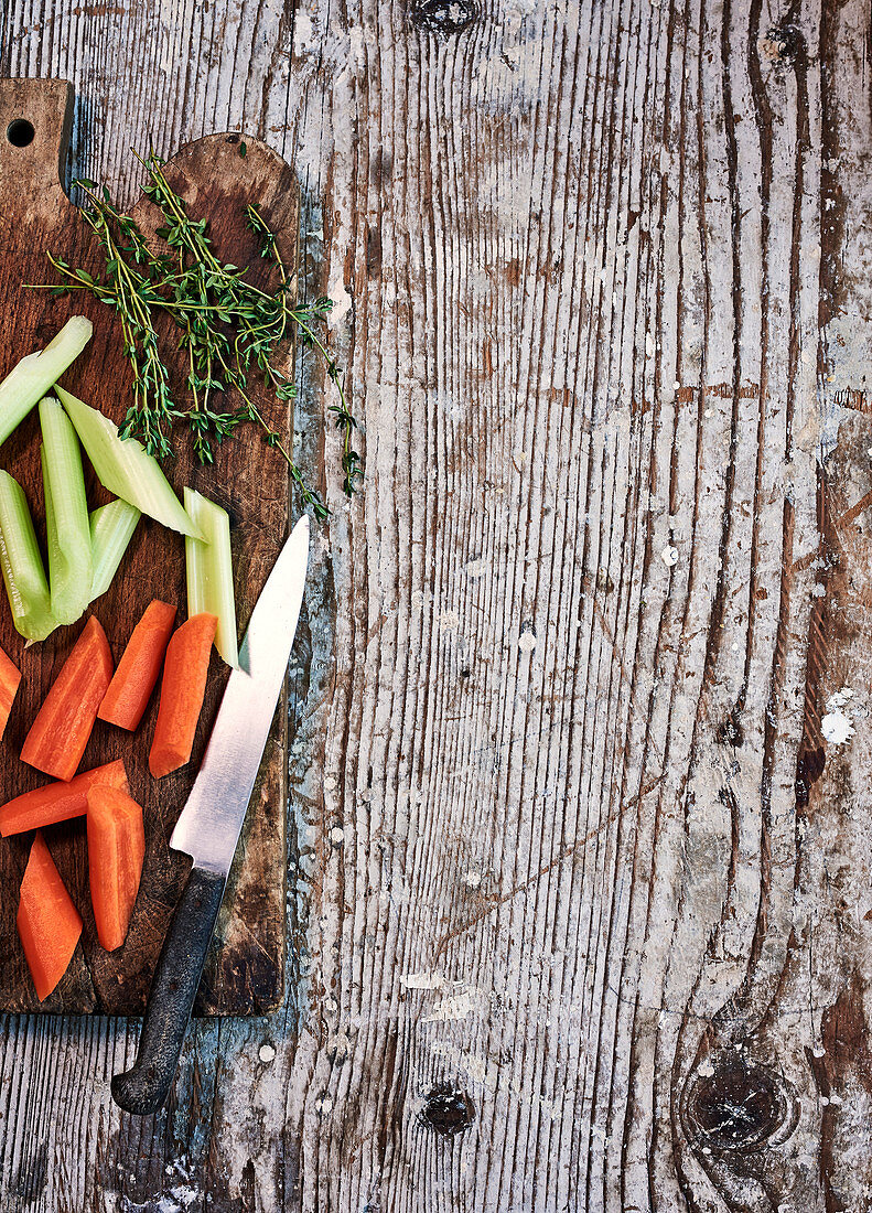 Karotten, Sellerie und Thymian auf Schneidebrett mit Messer