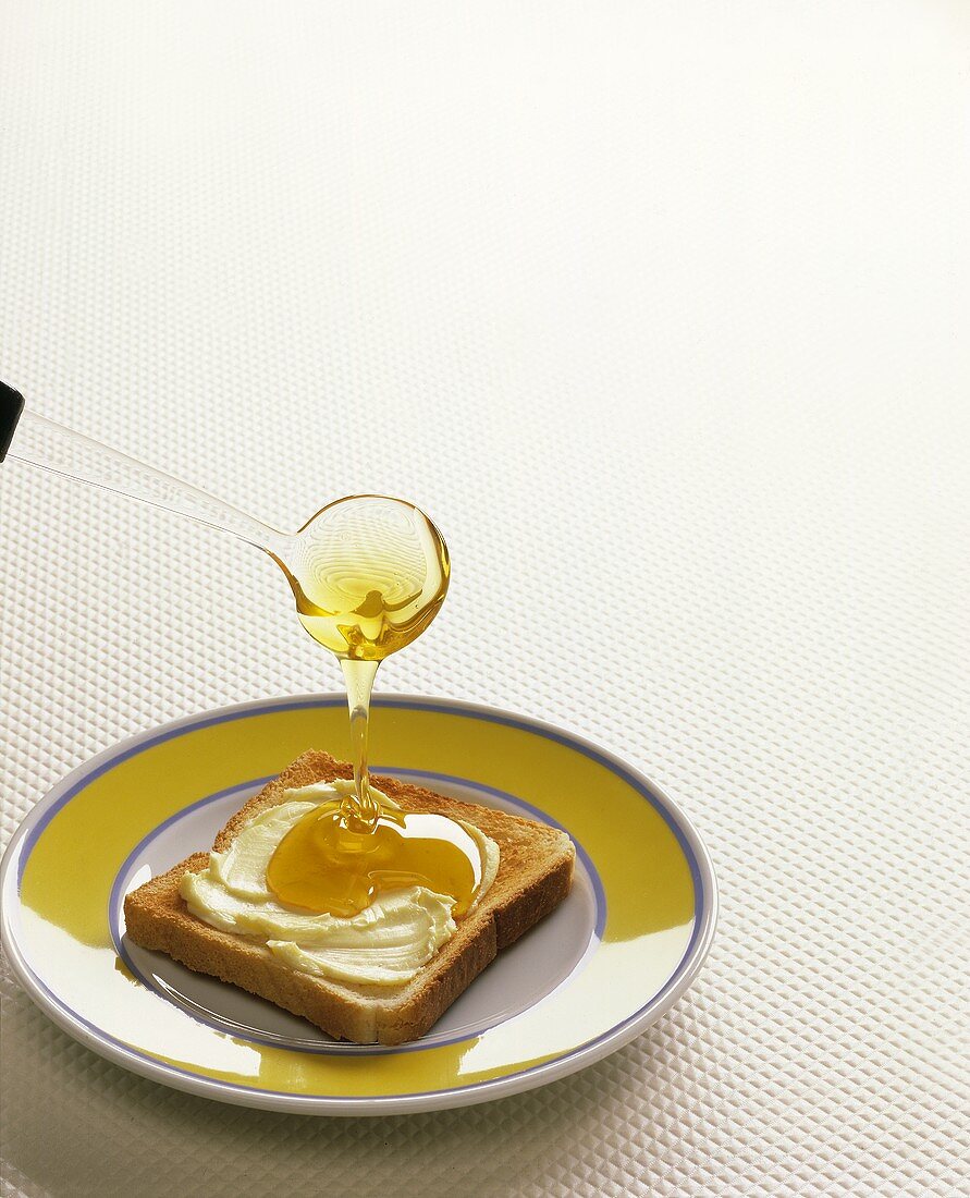Honig fließt von Löffel auf einen Toast mit Butter