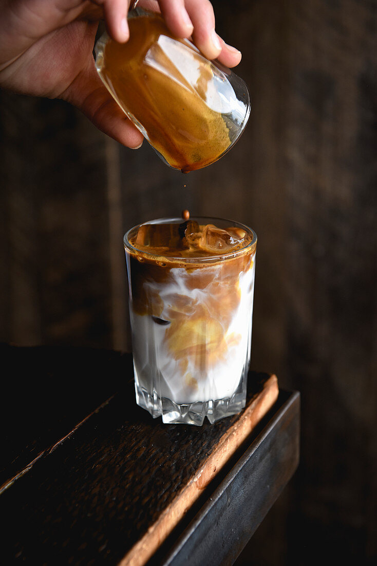 Pouring espresso for an iced latte into a glass with milk