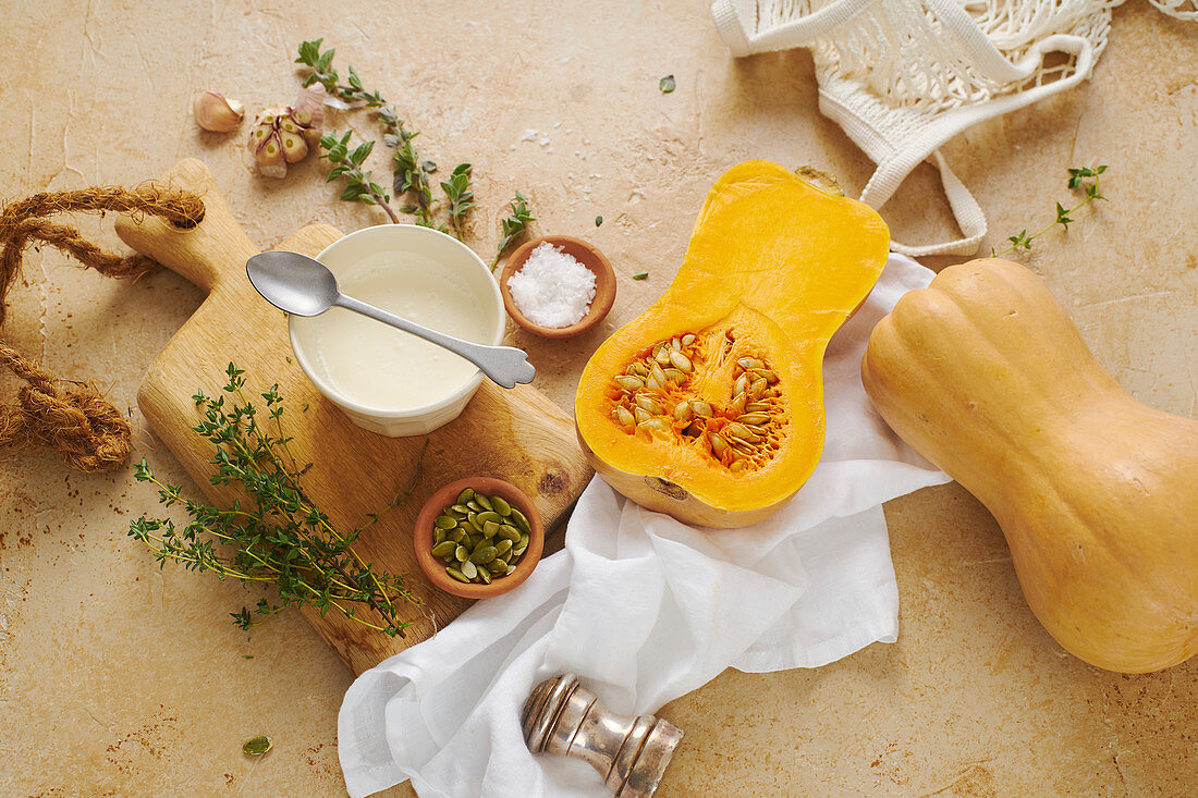 Halved butternut squash with cream, thyme and garlic on beige background. Ingredients for cooking dinner. Flatlay.