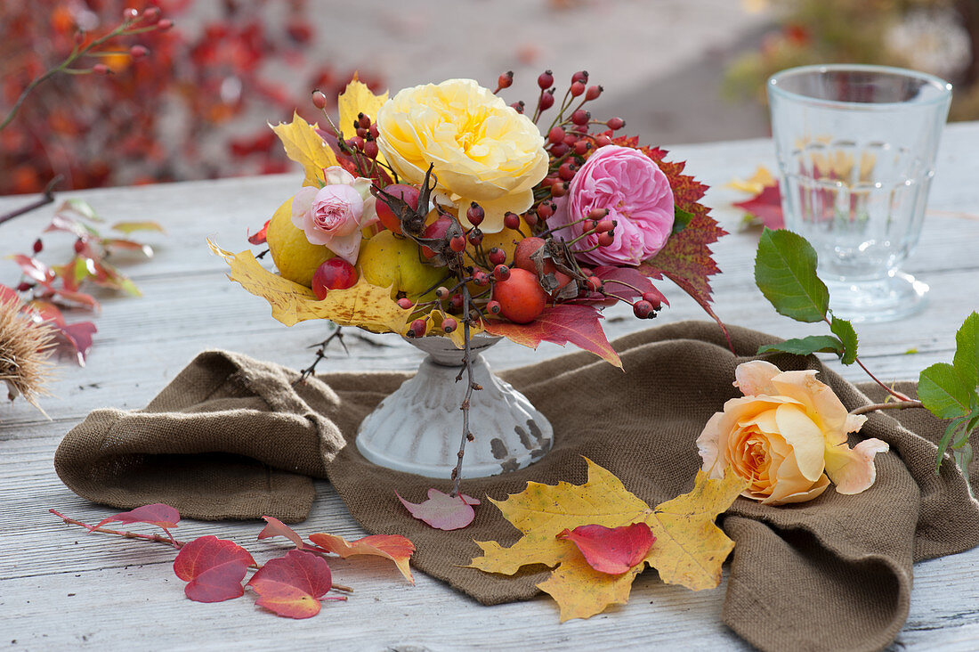 Small bouquet of roses with rose hips, decorative quinces and autumn leaves