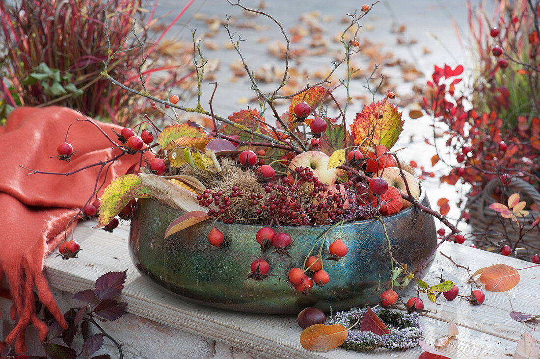 Bowl with autumn handicraft material: rose hips, twig, apples, autumn leaves, chestnuts, corn, wreaths made of heather