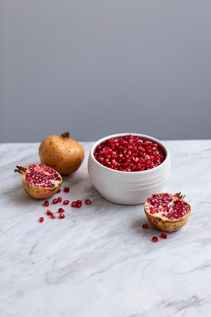 Pomegranate seeds in a ceramic bowl, with whole and halved pomegranates