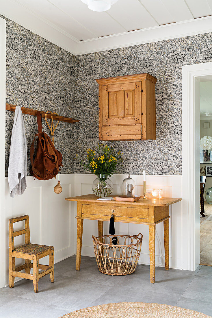 Wooden table below old wooden cabinet on wall with patterned wallpaper