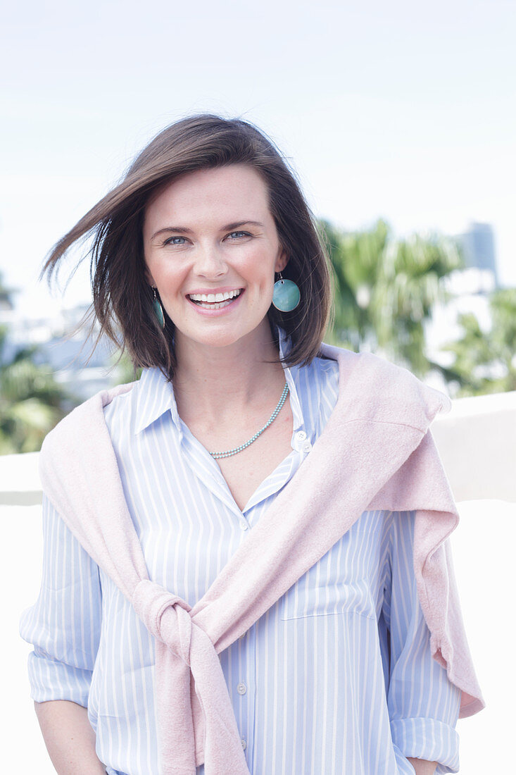 A young woman wearing a light, striped shirt with a jumper over her shoulders