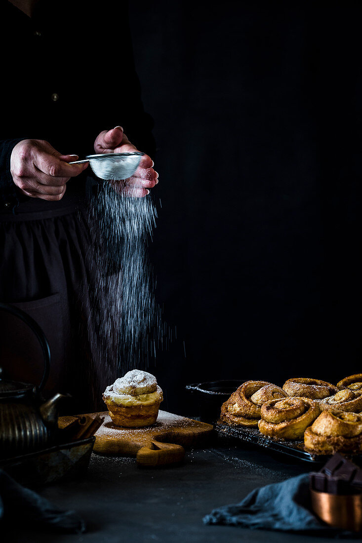 Cinnamon buns being dusted with icing sugar