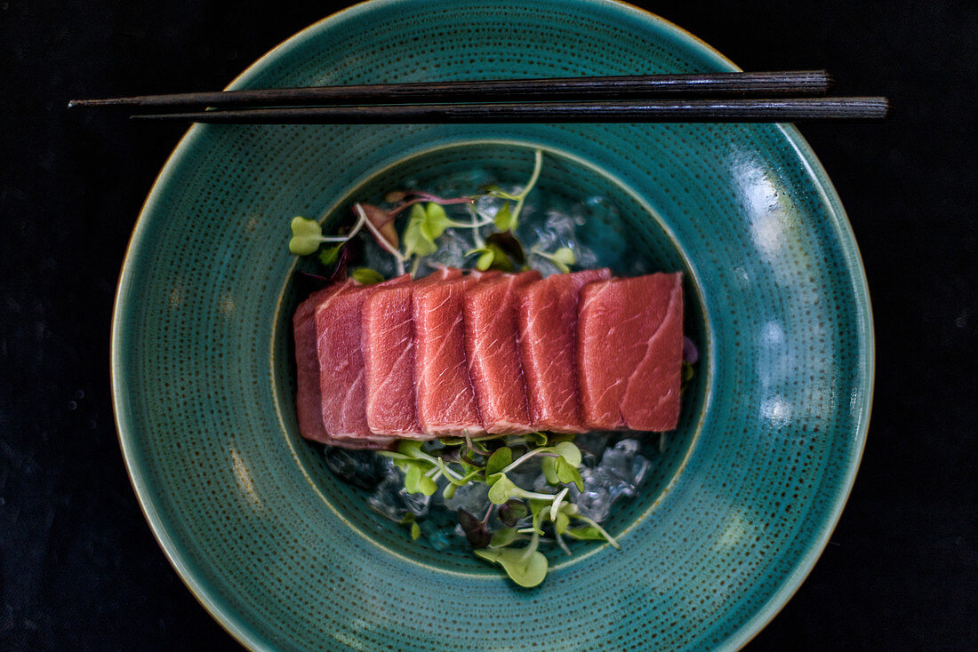 Palatable raw meat slices placed on plate with ice cubes and green herbs