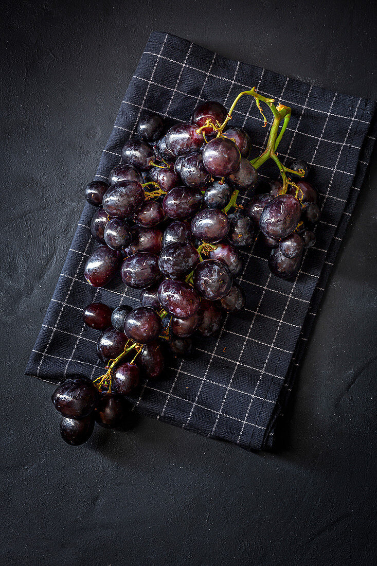 Bunch of delicious sweet ripe red grapes placed on checkered napkin on black surface