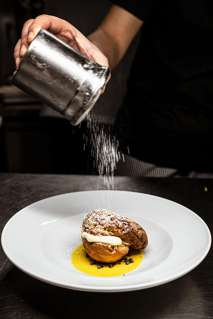 Unrecognizable chef spilling sweet powdered sugar of plate with yummy dessert in cafe kitchen