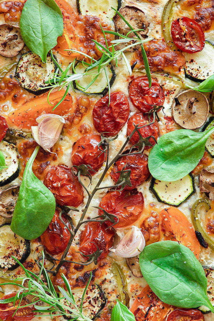 Palatable vegetarian pizza with cherry tomatoes and mushrooms garnished with fresh basil and rosemary