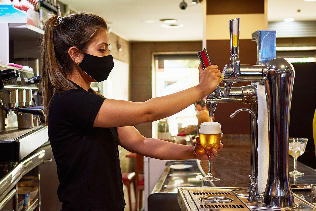 Barfrau mit Schutzmaske beim Zapfen von Bier