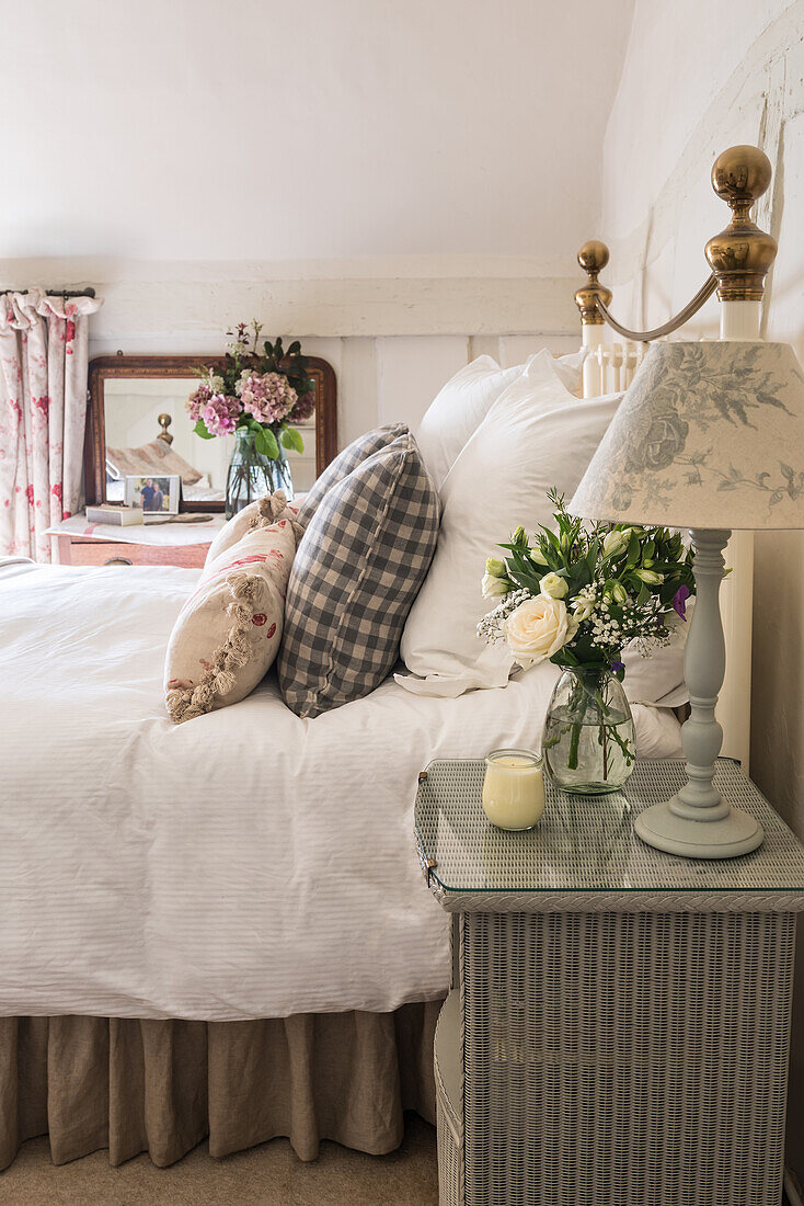 Lamp and bouquet of roses on bedside table next to wrought-iron bed in bedroom